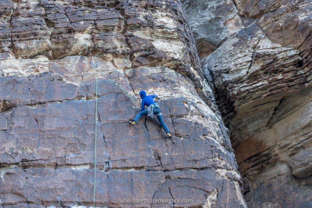 Rock climber on wall with ropes wearing blue hoodie and grey pants mid move