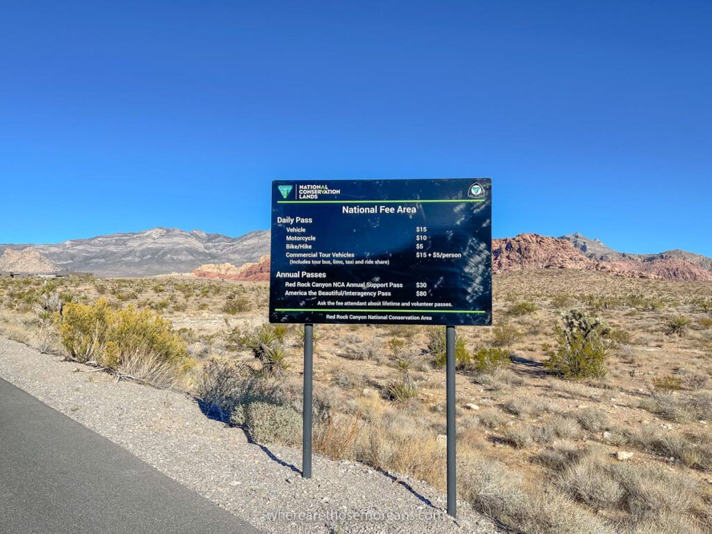 Sign with entry fees and passes accepted on roadside with blue sky background in desert environment