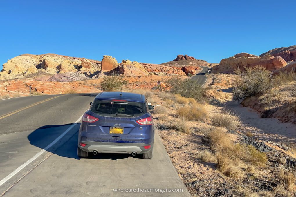 Small parking space on the side of a road with blue car parked in a red rock landscape