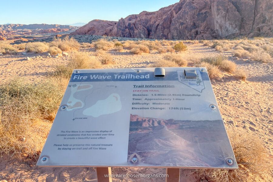 Sign marking the beginning of a hike with sun lighting up sand and rocks
