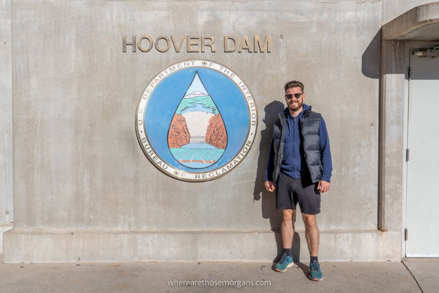 Man stood with Hoover Dam emblem and sign on a day trip from Las Vegas Nevada
