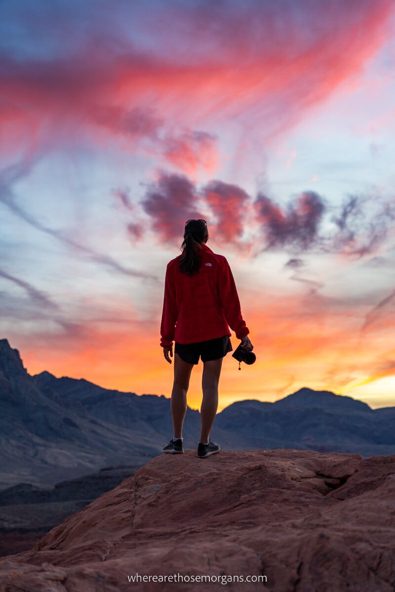 Woman stood on rock with distant mountains and stunning colors in the sky at sunset