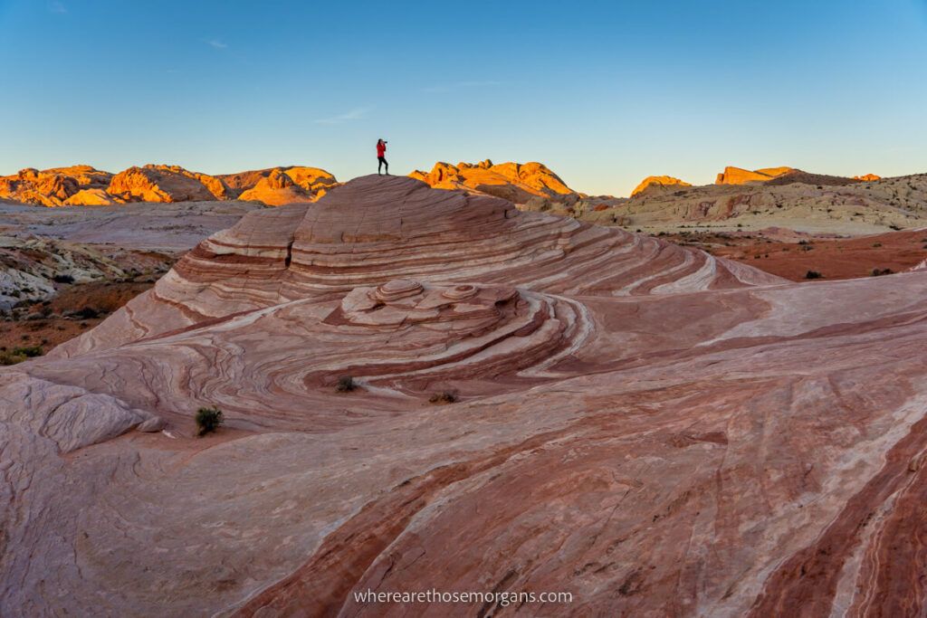 Hiker with camera stood on the top of a dome at Fire Wave at sunrise in Valley of Fire State Park near Las Vegas Nevada