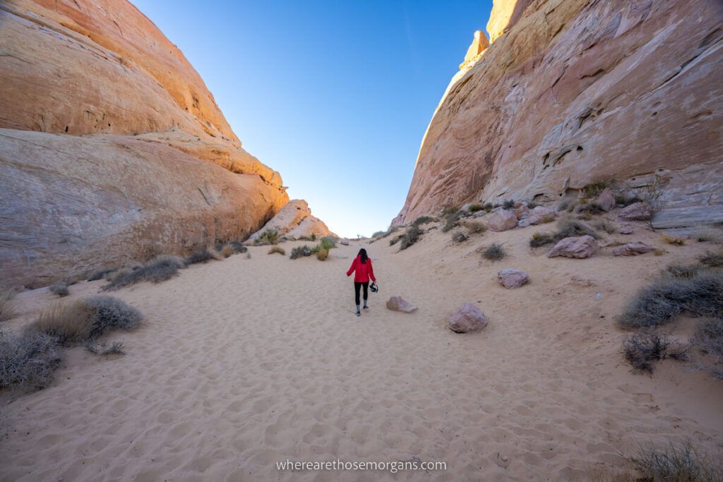 Woman hiking a deep sand trail through tall canyon walls towards blue sky