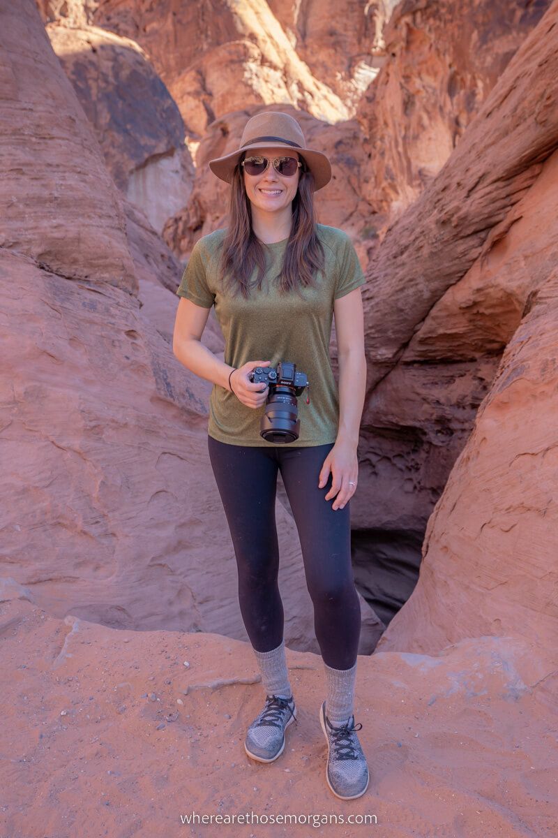 Hiker with camera stood in front of a hole in red sandstone rock