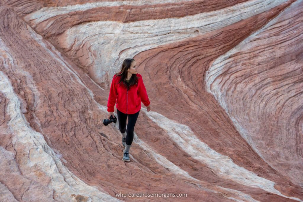 Kristen from Where Are Those Morgans hiking Fire Wave with a camera and red fleece at sunrise in Valley of Fire State Park near Las Vegas in Nevada on swirling smooth red and white sandstone