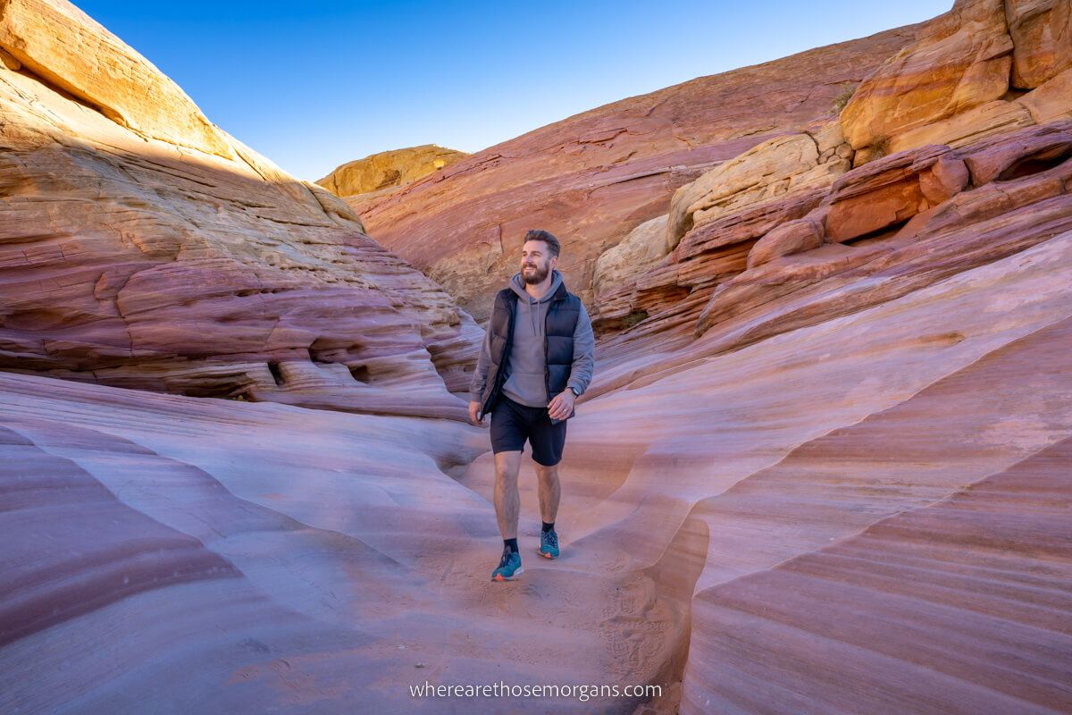 Mark from Where Are Those Morgans hiking through Pink Canyon in Valley of Fire State Park with shadows inside the canyon and sunlight above the canyon walls vibrant colors in the sandstone