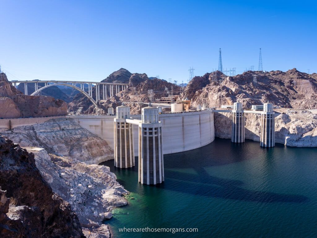 Hoover Dam from behind with four towers and water foreground and memorial bridge in background one of the easiest and most popular Las Vegas day trips