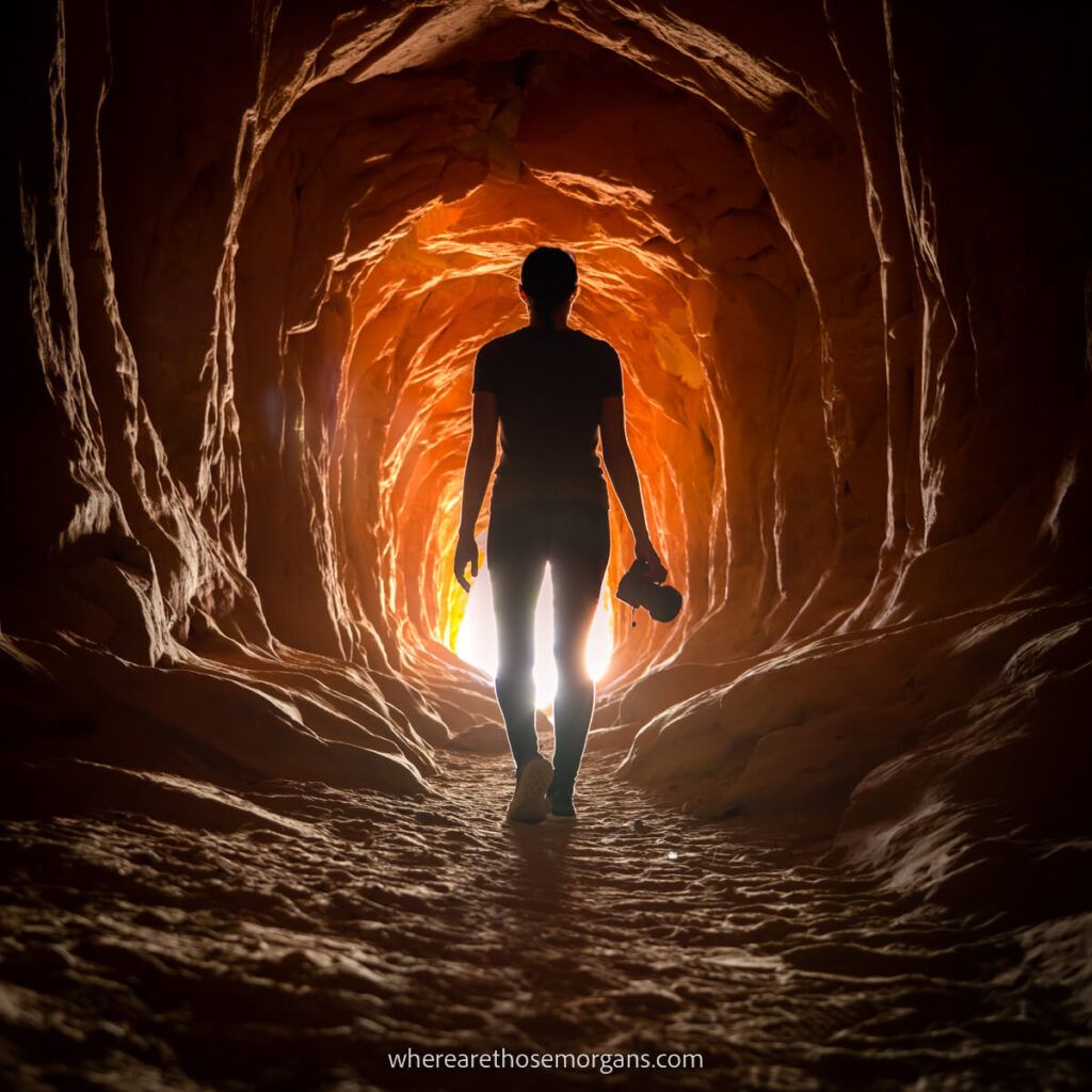 Woman walking through dark tunnel with light opening at the end silhouetted with camera