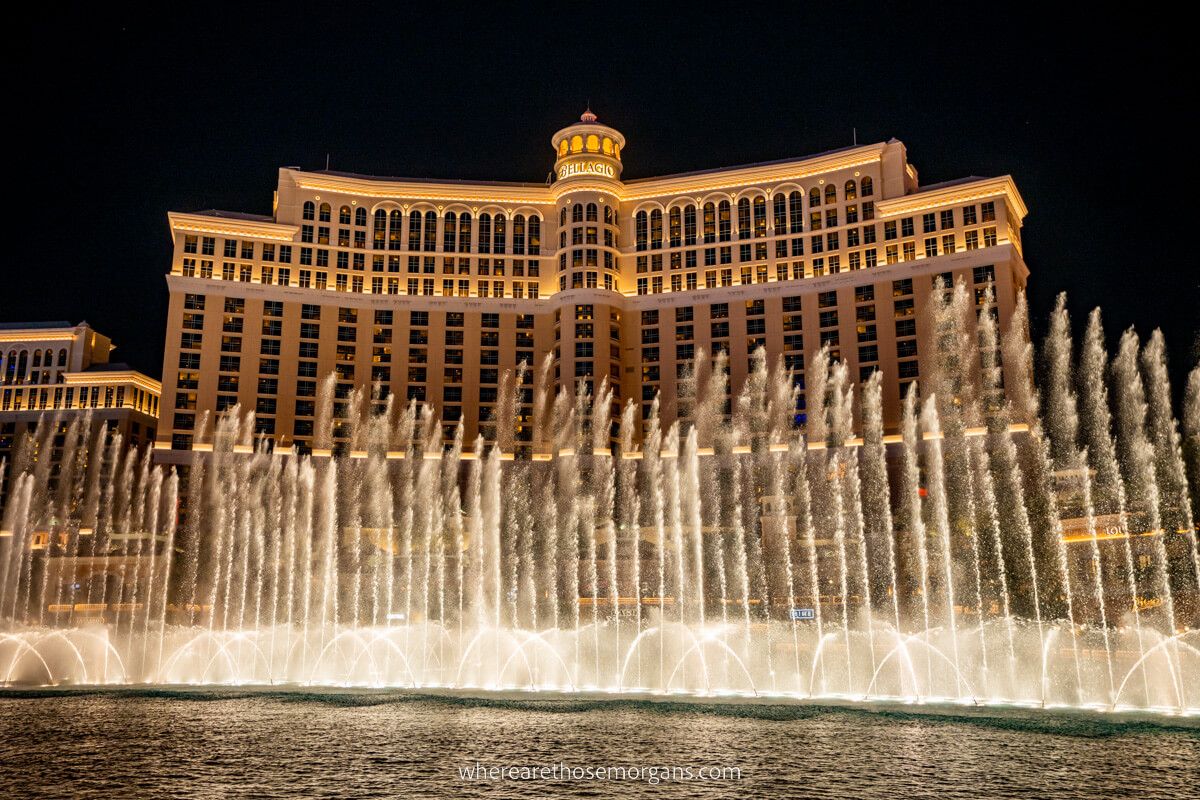 Bellagio fountain display water jets in a long line bursting into the sky with the hotel in the background at night