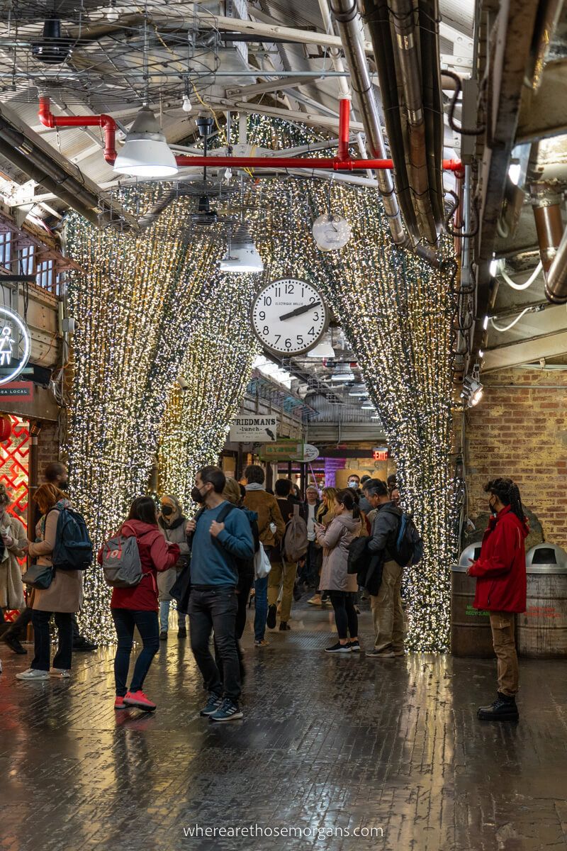 Ornate and colorful curtains leading through Chelsea Market with people looking at shops and a big clock