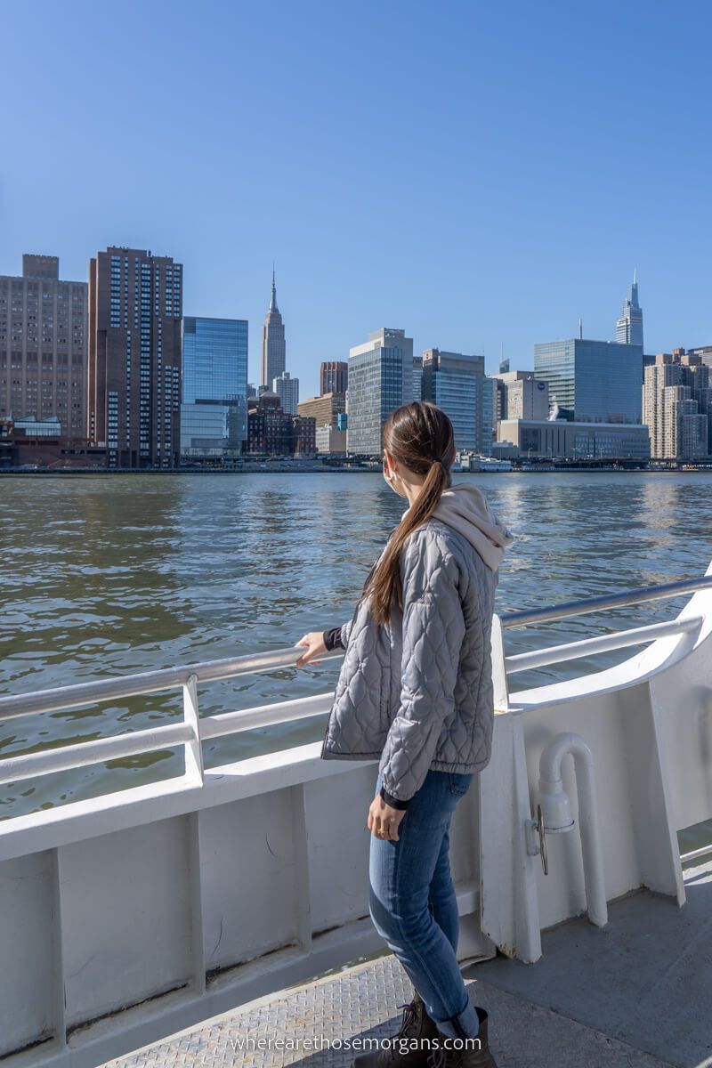 Woman standing on a boat looking out across river to buildings in nyc
