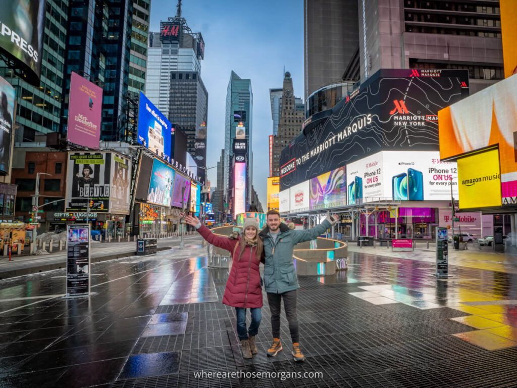 Couple taking photo with arms outstretched in Times Square NYC with bright lights and no people