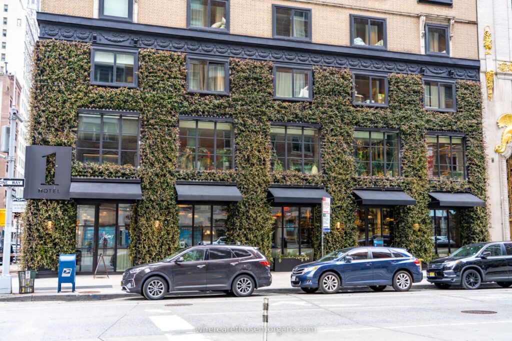 1 Hotel in Central Park from outside with moss and vines growing up the exterior and cars parked on a road out front
