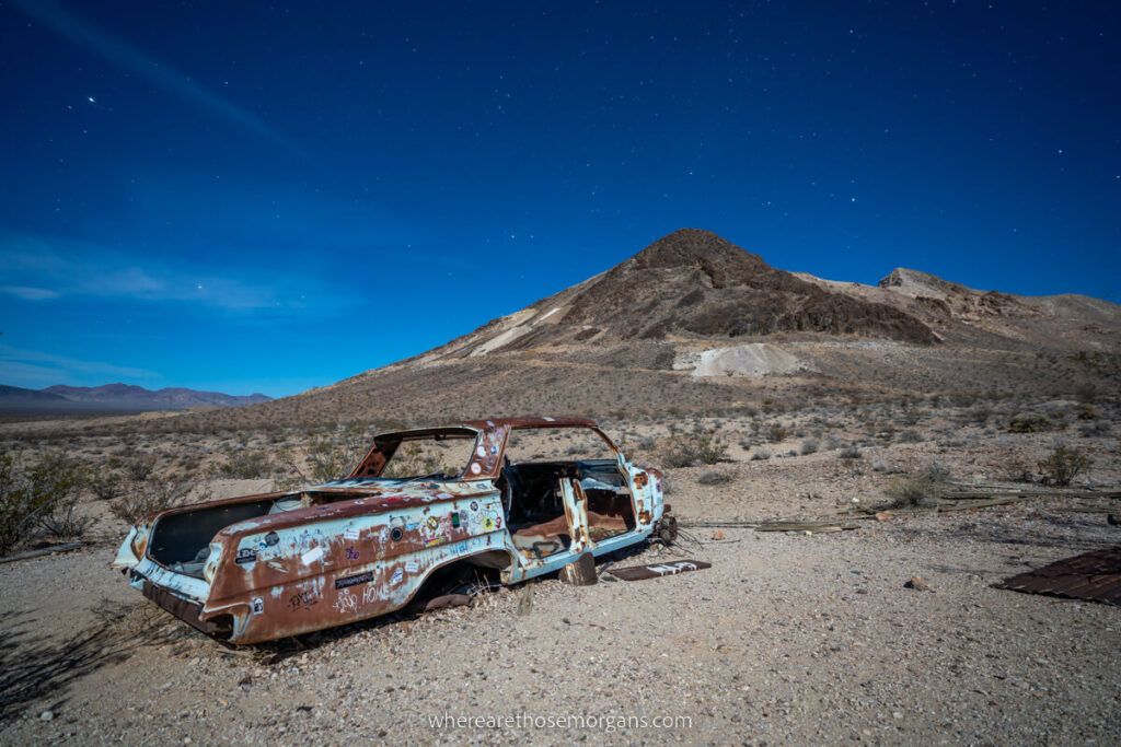 Abandoned old car in a barren and desolate landscape at night with bright blue sky from moonlight