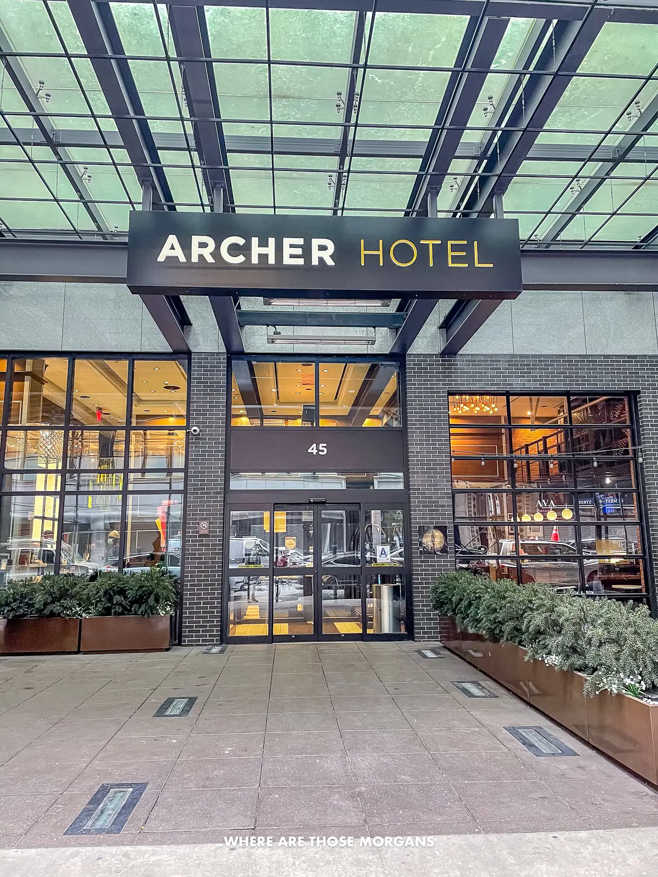 Entrance to the Archer Hotel in NYC with the hotel name above glass doors and below a glass overhang