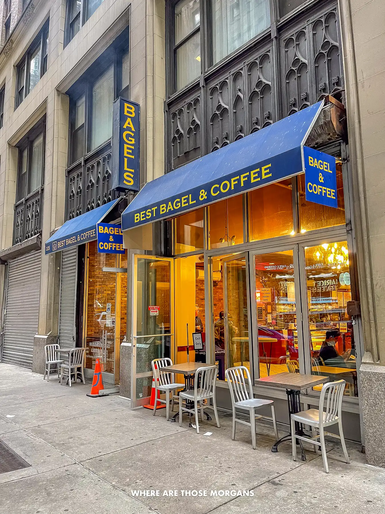Exterior photo of Best Bagel and Coffee on 35th street in NYC with a few small tables and chairs outside the entrance but no people
