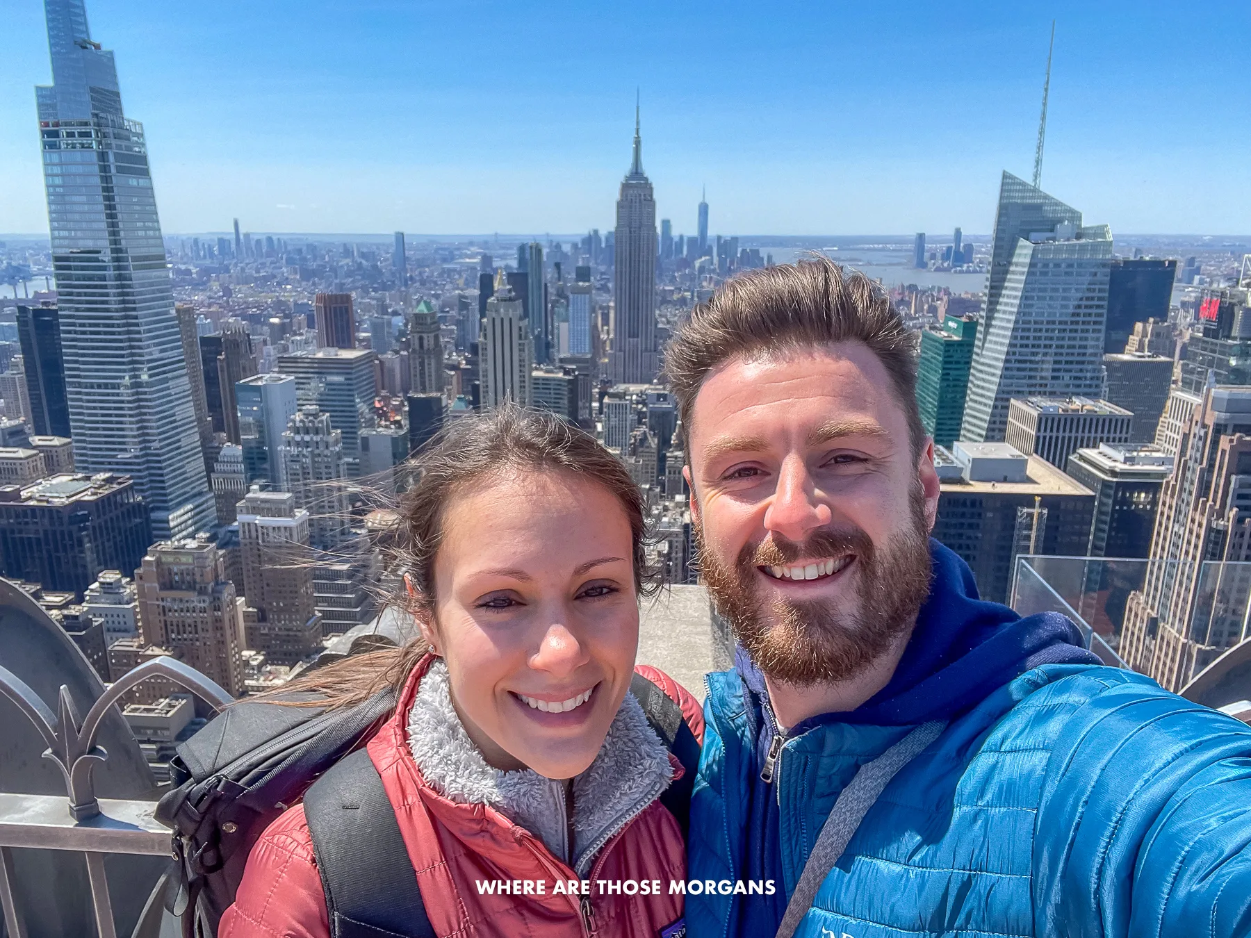 Mark and Kristen from Where Are Those Morgans taking a selfie in coats on a sunny but very windy day at Top of the Rock in New York in the spring