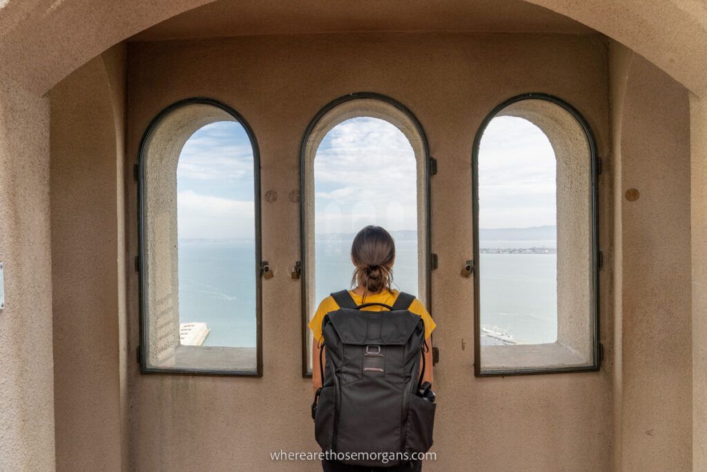 Woman at the top of Coit Tower looking through three arched windows at the Bay