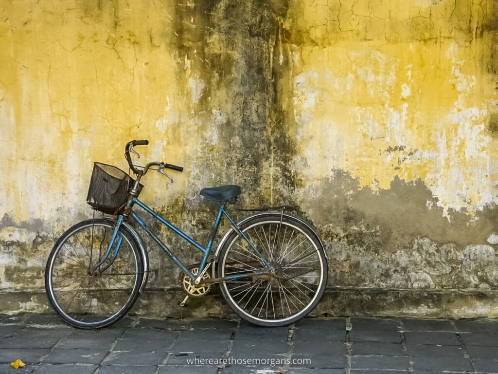 An old blue bicycle with basket parked against a yellow wall in Hoi An ancient town