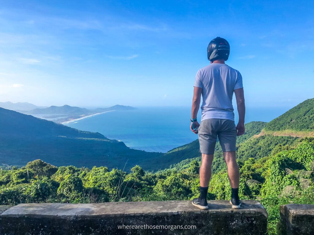 Man standing on a rock wall looking out at views of the Hai Van Pass