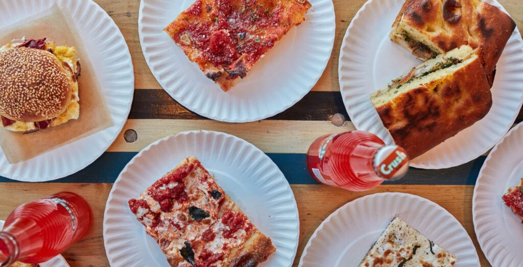 Pieces of pizza on paper plates with red crush soda