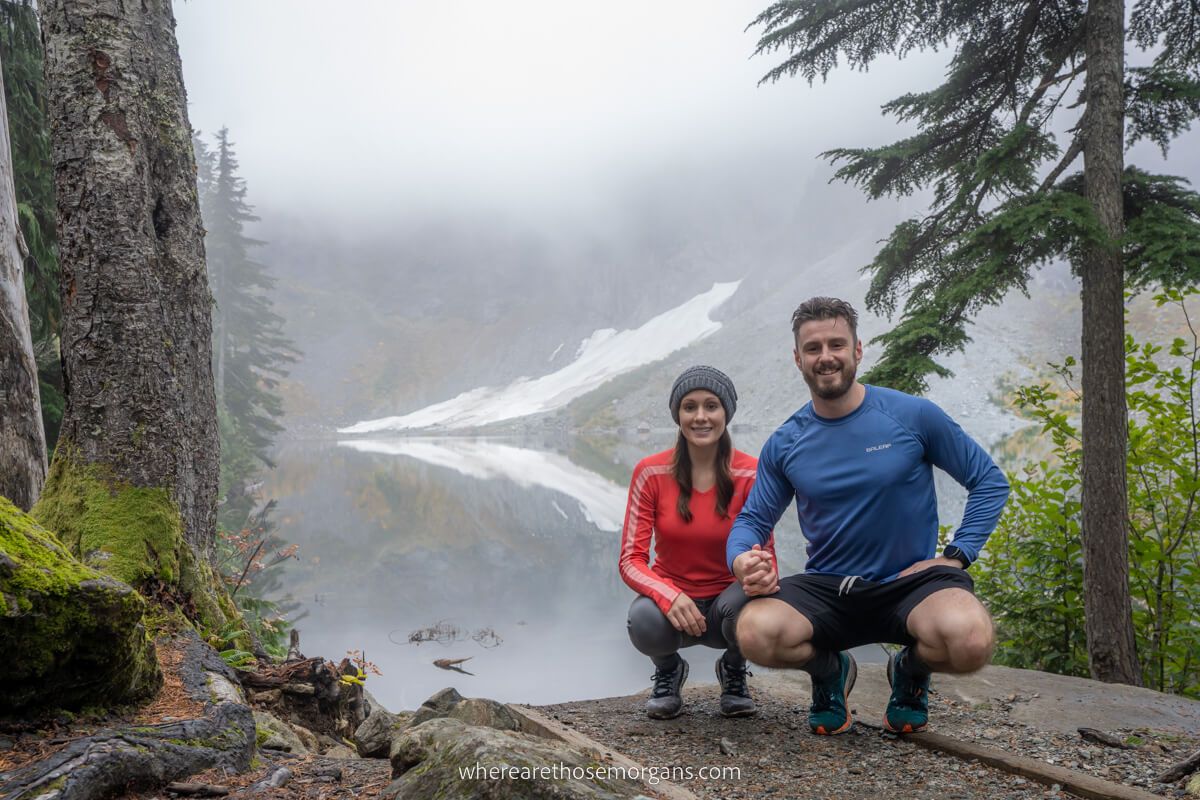 Mark and Kristen Morgan from Where Are Those Morgans crouched on knees for a photo with Lake Serene on a misty day in Washington