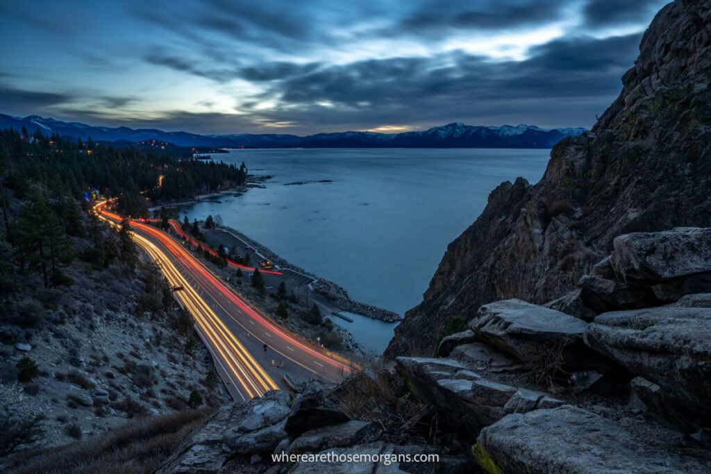 White and red car light trails at night entering a tunnel with a lake in the background