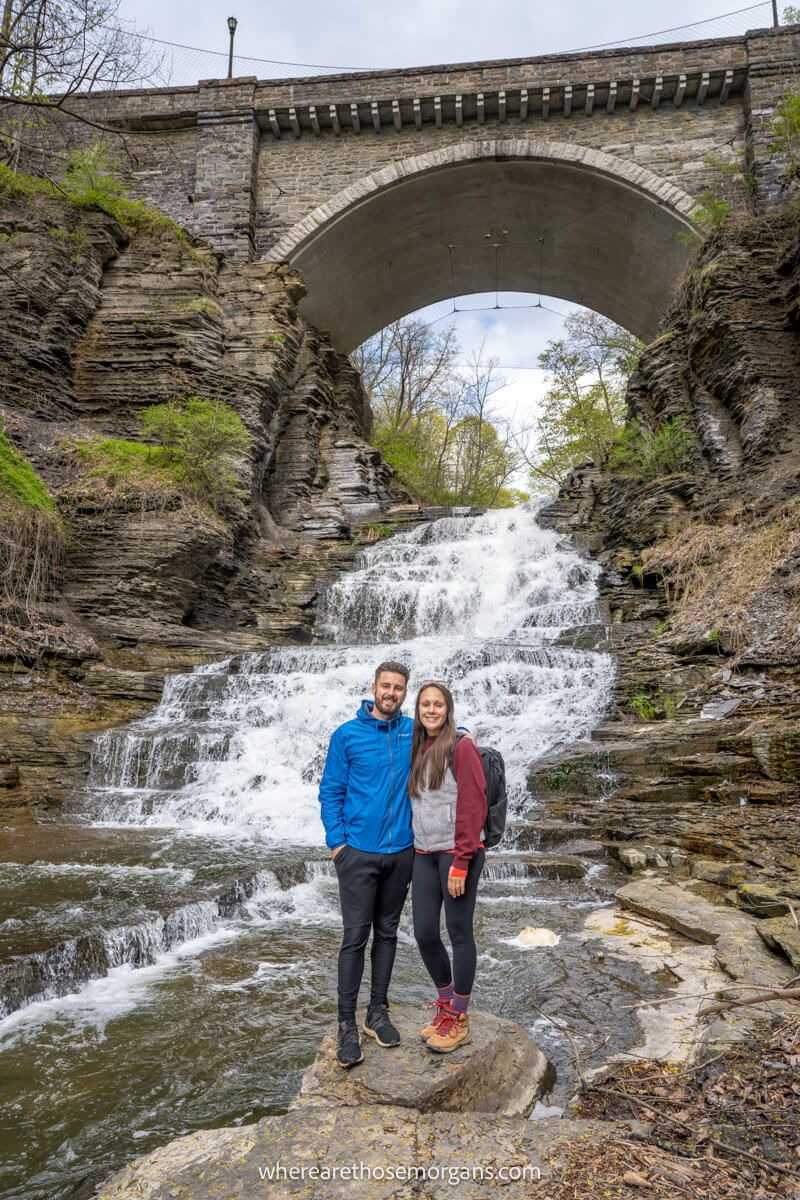 Mark and Kristen Morgan from Where Are Those Morgans standing in front of a waterfall in the Cascadilla Gorge Trail in Ithaca NY