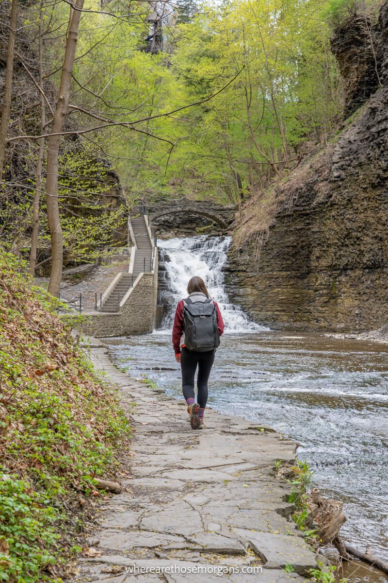 Hiker walking along a path next to a creek with steps and waterfalls ahead