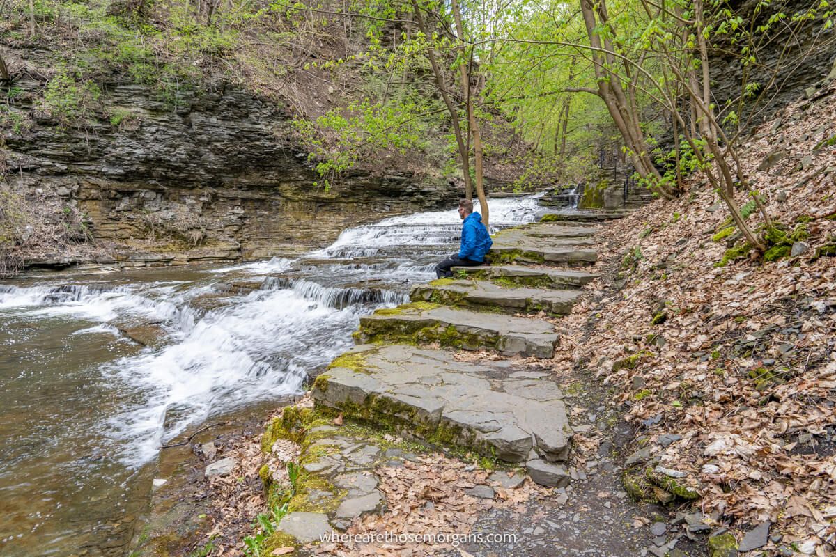 Hiker sat on stone steps enjoying the view into waterfalls hiking along the Cascadilla Gorge Trail in Ithaca NY