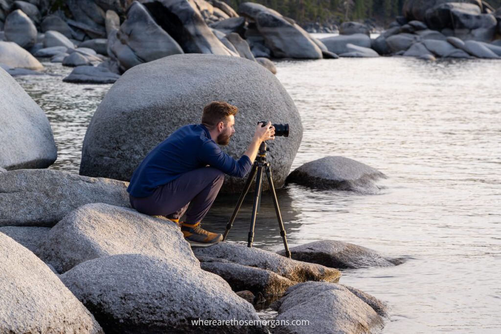 Photographe accroupi sur des rochers lisses avec trépied et appareil photo au crépuscule