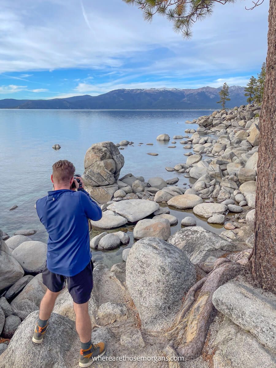 Photographer stood on boulders taking a photo of a rocky shoreline