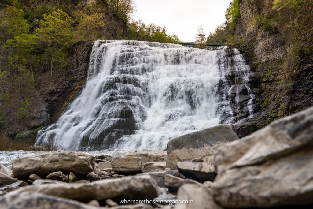 Tall and wide waterfall flowing heavily behind small boulders in the foreground in Ithaca Falls NY