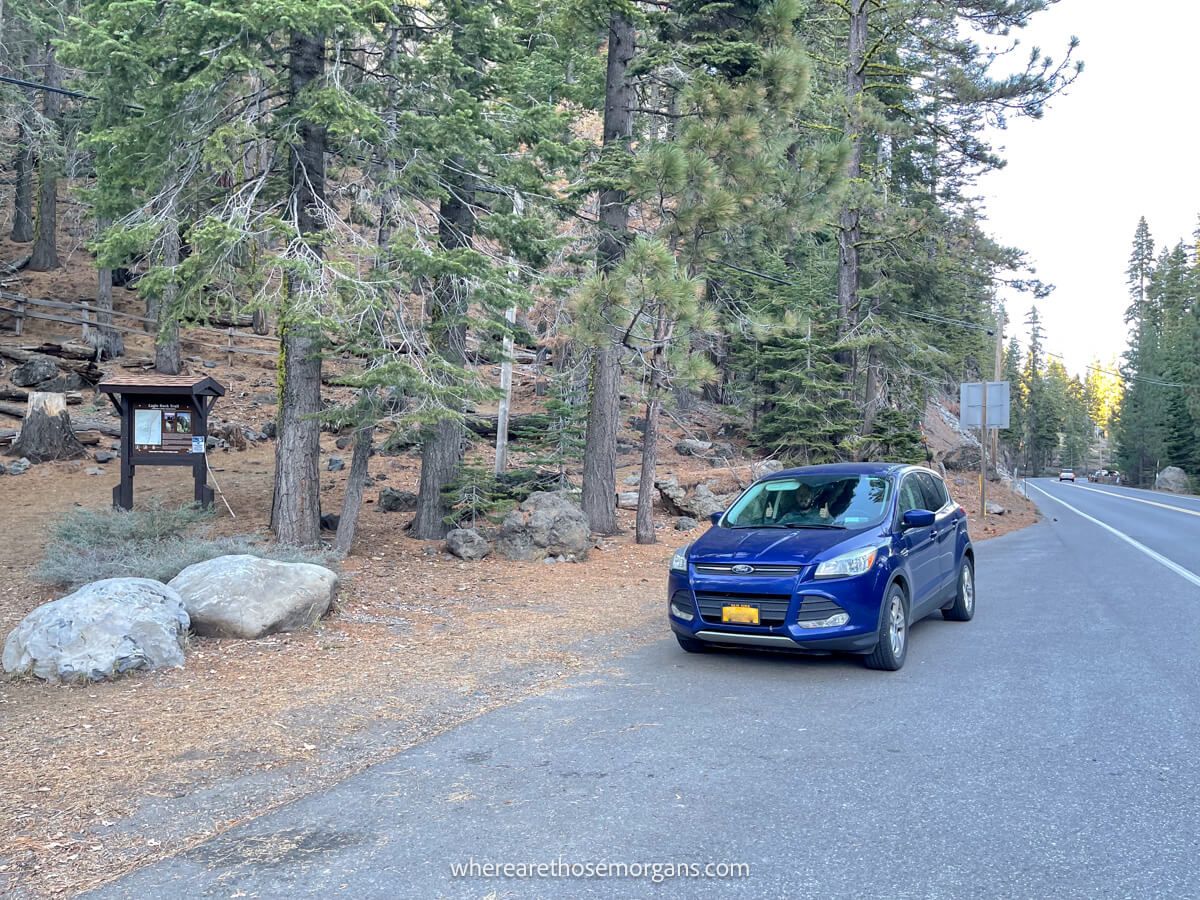 Blue car parked in a roadside lot near a trailhead