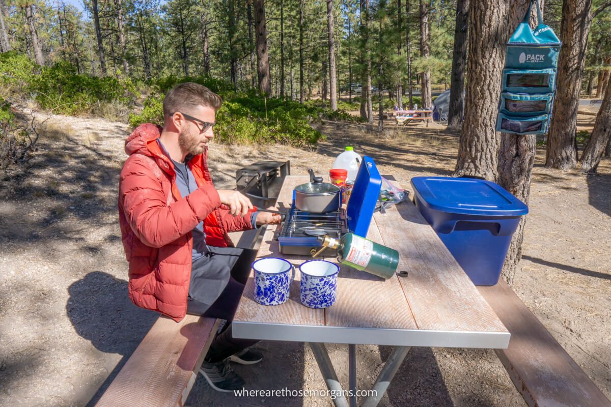 Person cooking food on a small gas stove at a bench in Bryce Canyon campground on a sunny day