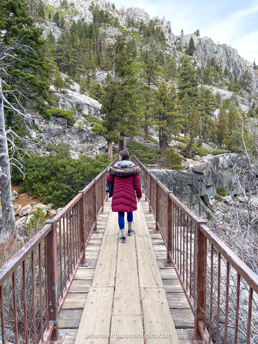 Hiker in maroon winter coat walking over a wooden and metal bridge