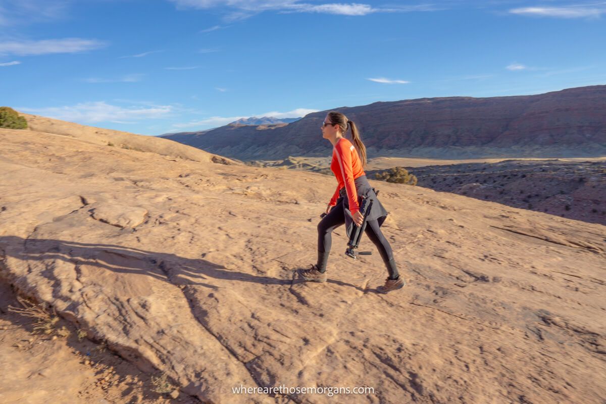 Hiker walking up a steep trail made of sandstone with a tripod in hand