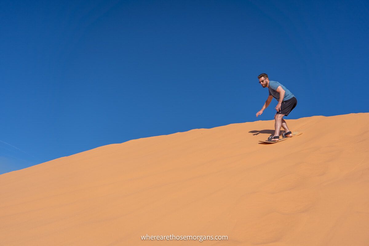 Person sandboarding down a giant sand dune with deep blue sky on a road trip through Utah