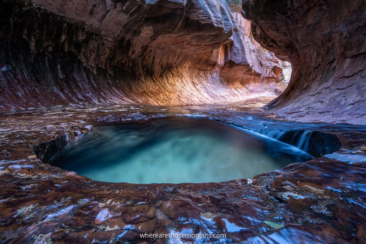 Unique tunnel like rock formation with orange light glowing and shallow emerald colored pools in The Subway in Zion