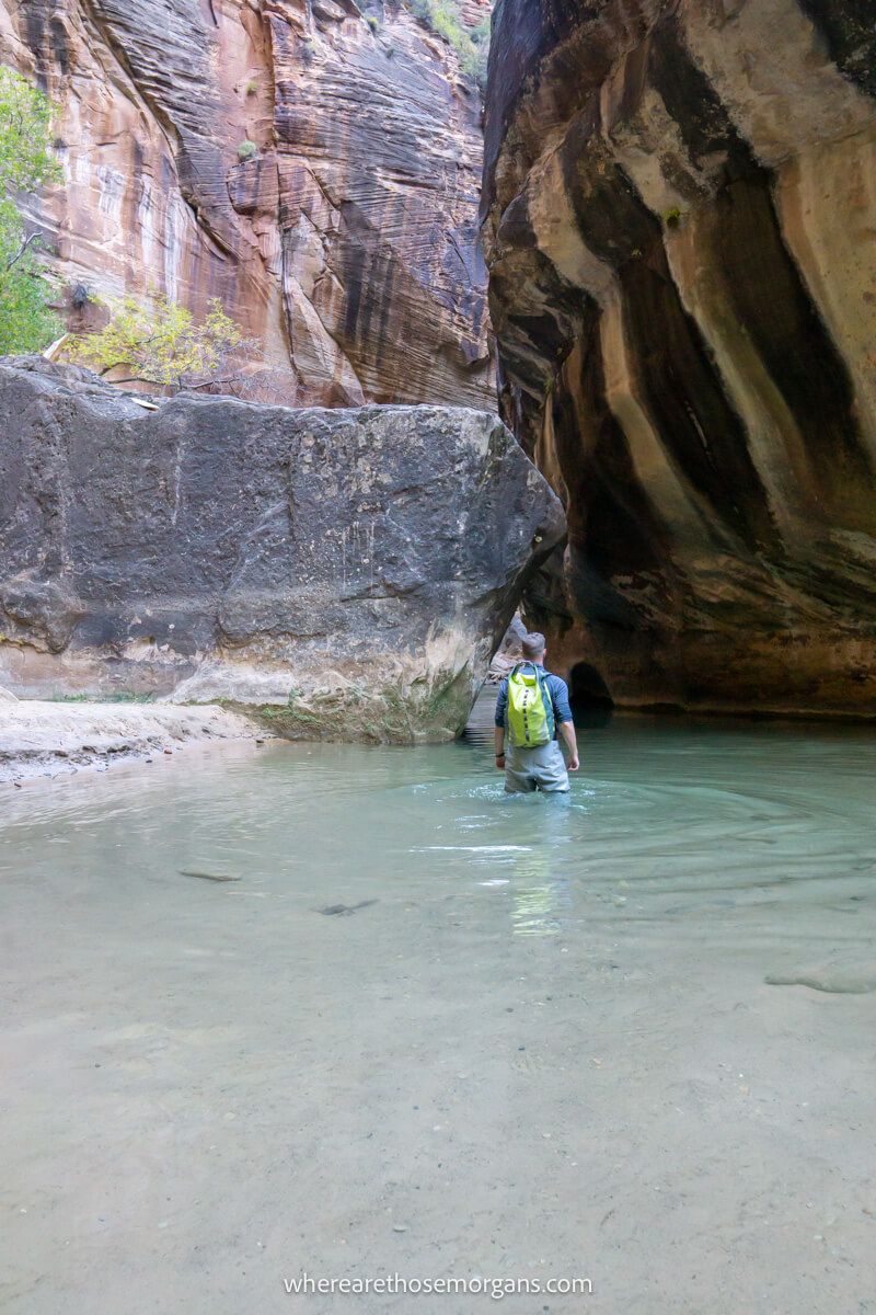 Person hiking through waist deep water with waterproof backpack in a narrow canyon