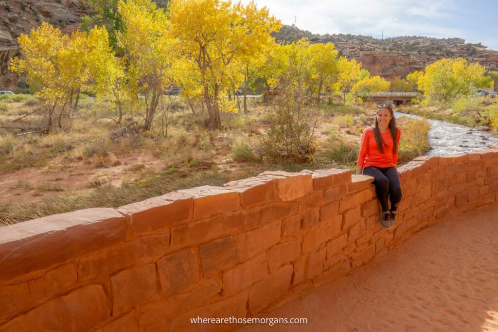 Woman sitting on a rock wall in Capitol Reef National Park with bright yellow trees in the background