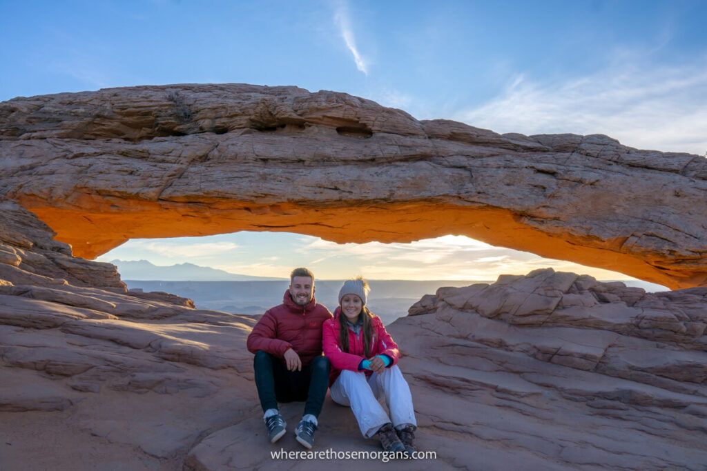 Hikers sat on rocks with an arch and distant landscape behind