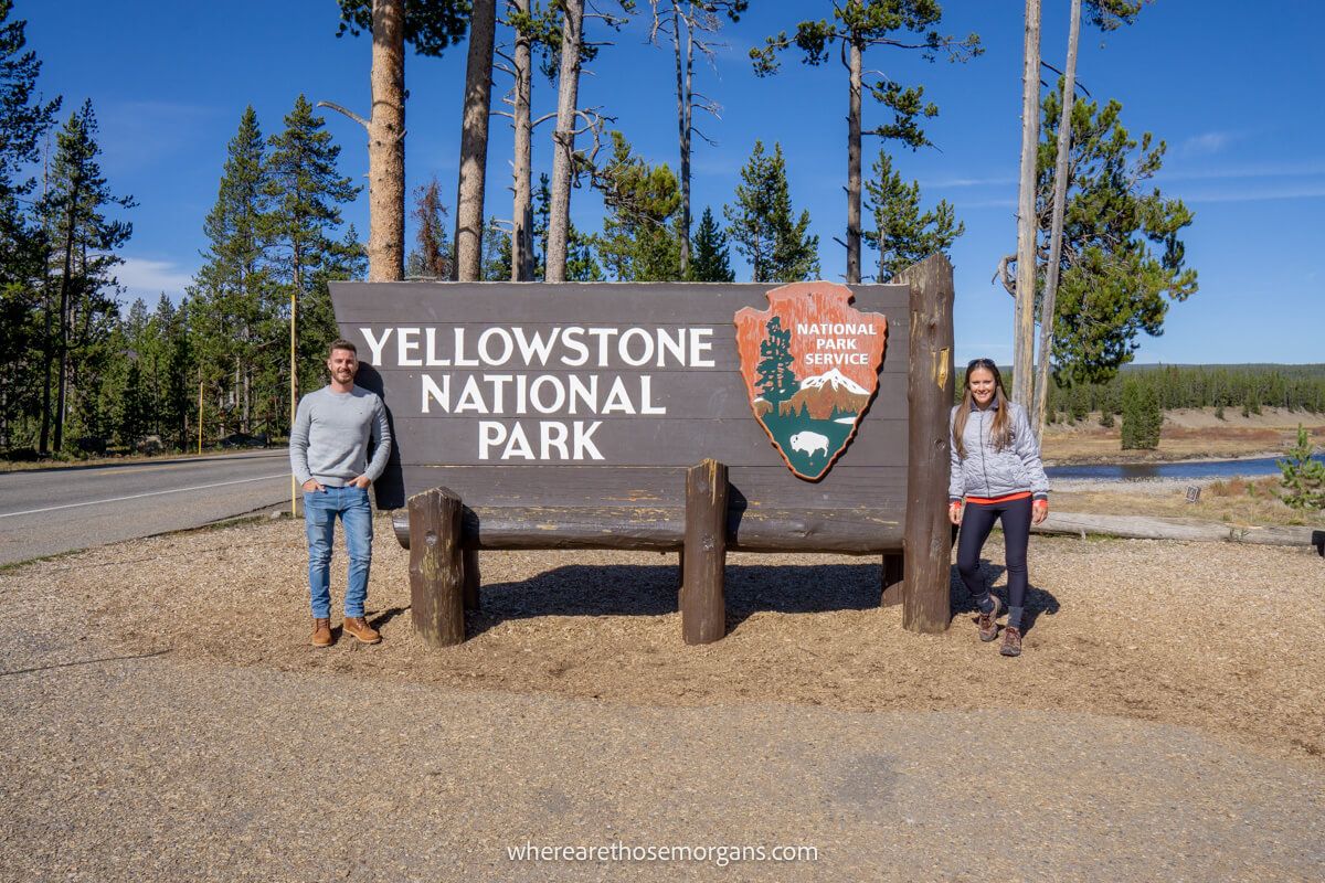 Man and woman posing for a photo at the Yellowstone National Park sign