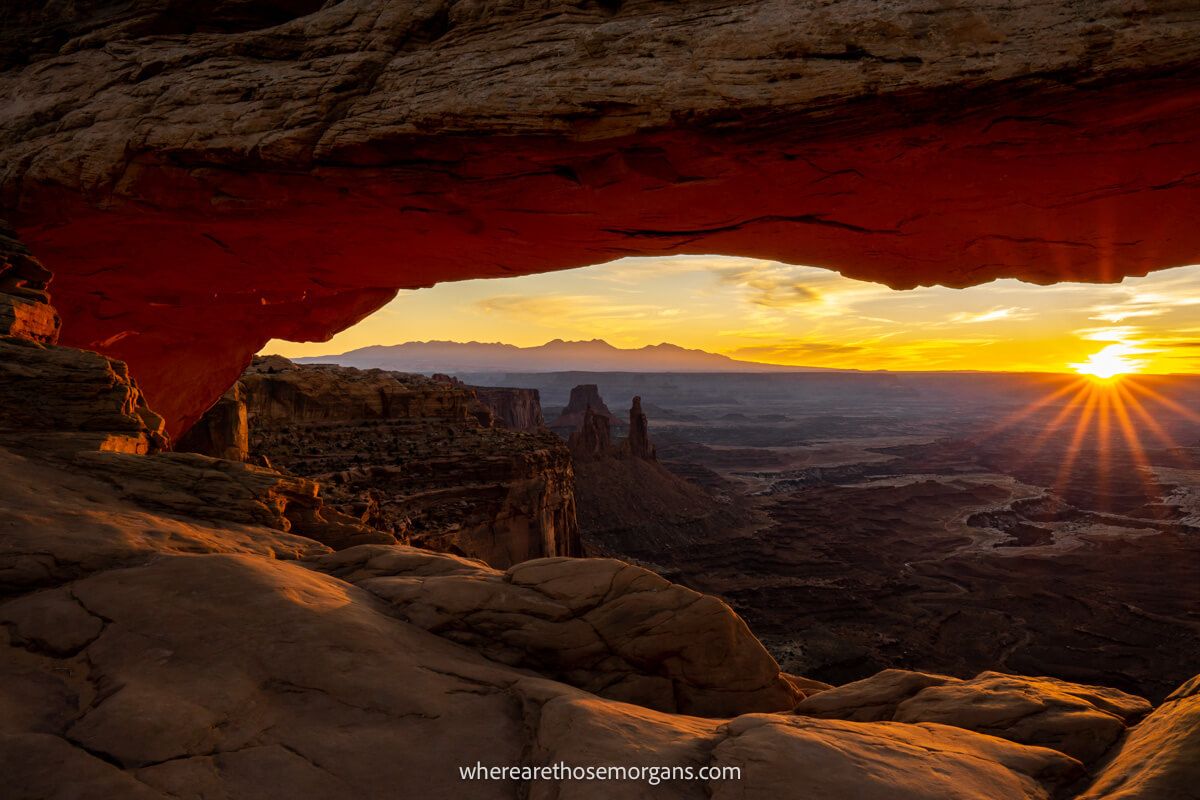 Sunrise over a distant horizon with arch in the foreground lit up red