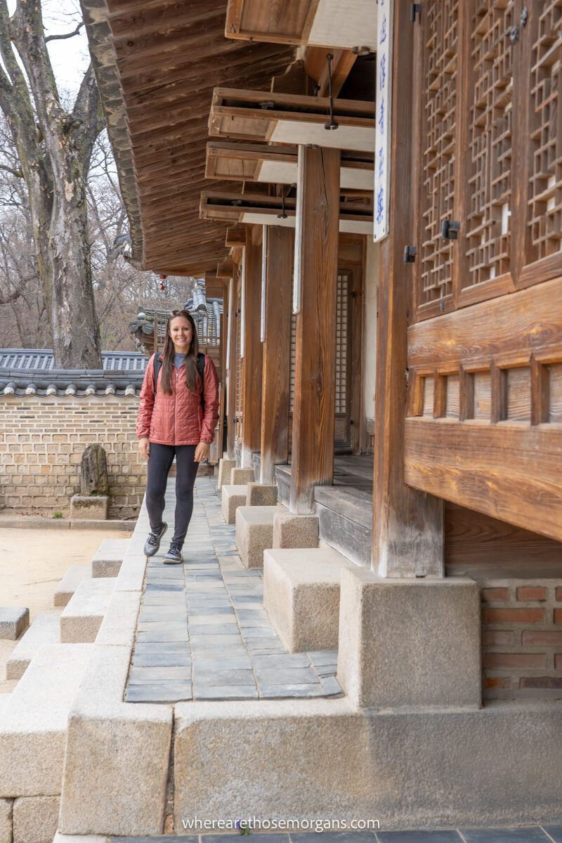 Woman walking next to a wooden building in Huwon Secret Garden