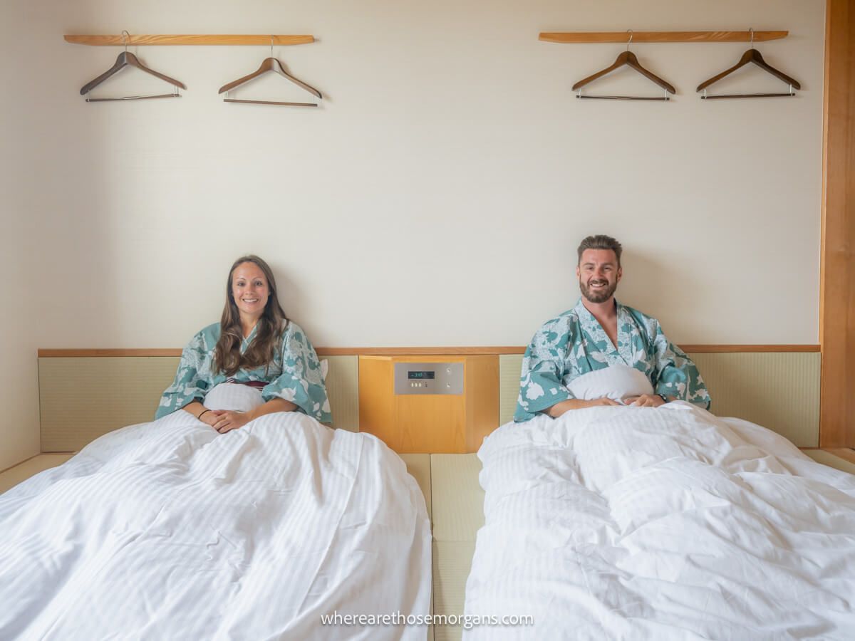 Couple sitting up in two beds next to each other on the floor in a traditional Japanese hotel room in Hakone with yukata on