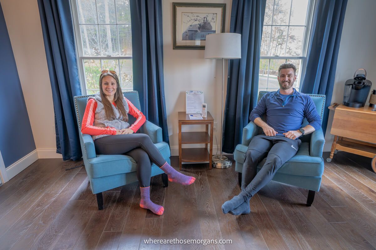 Couple sat next to each other in armchairs inside a hotel in upstate New York with wooden floor and curtains open