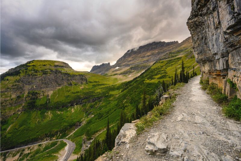 Hiking High Line trail in Glacier National Park with stunning views over green vegetation from the narrow path