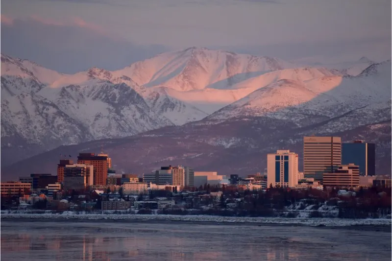 Mountains glowing at sunrise pink in Anchorage Alaksa with city and sea in foreground